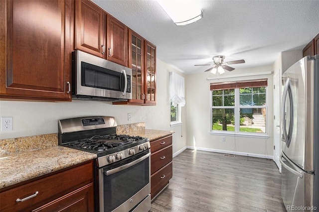 22002 E Irish Dr, Aurora, CO 80016 - kitchen with appliances with stainless steel finishes, dark wood-style floors, ceiling fan, glass insert cabinets, and light stone countertops