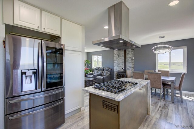 45321 Summit Rd, Parker, CO 80138 - kitchen featuring appliances with stainless steel finishes, island range hood, light wood-style flooring, white cabinetry, and light stone countertops