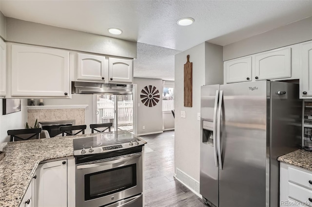 kitchen featuring a textured ceiling, wood finished floors, white cabinetry, appliances with stainless steel finishes, and light stone countertops