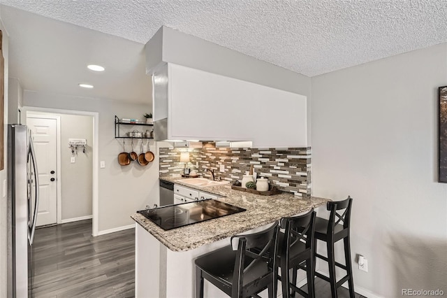 kitchen featuring a peninsula, stainless steel appliances, a sink, a kitchen bar, and backsplash