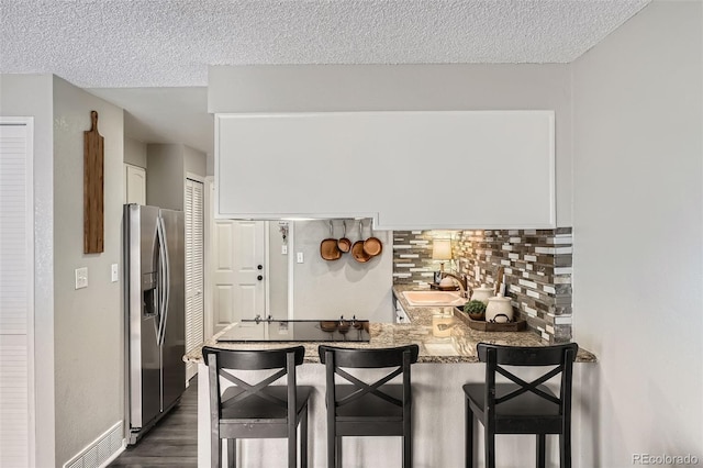 kitchen featuring a sink, backsplash, stainless steel fridge, white cabinets, and dark wood-style flooring