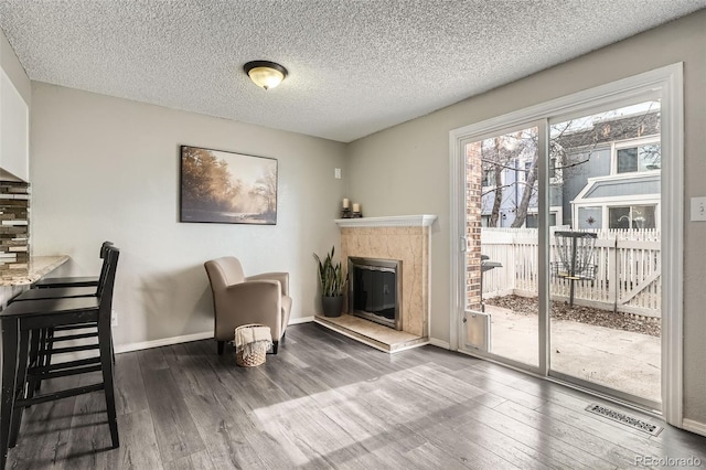 interior space with visible vents, baseboards, a tile fireplace, wood finished floors, and a textured ceiling