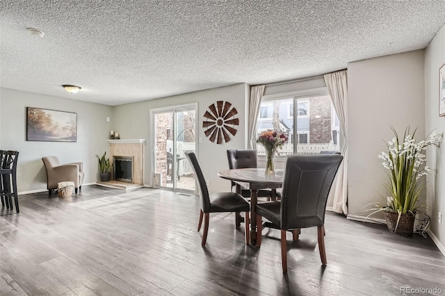 dining room featuring a glass covered fireplace, a textured ceiling, baseboards, and wood finished floors