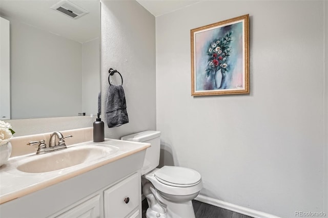 bathroom featuring visible vents, baseboards, toilet, wood finished floors, and vanity