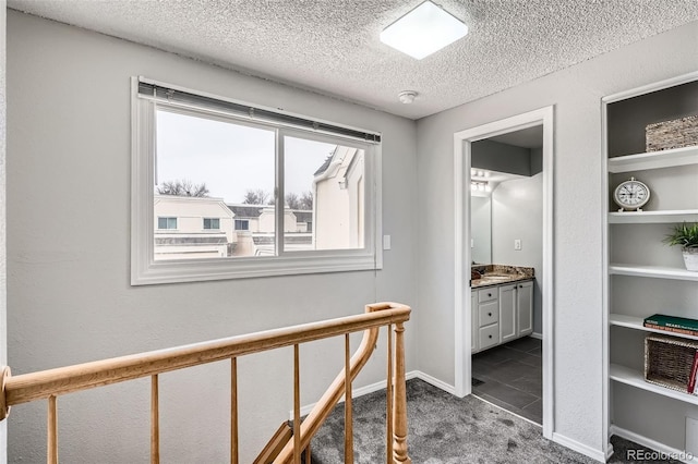 hallway with dark carpet, a textured ceiling, and baseboards