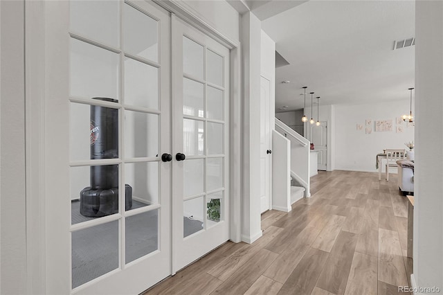 corridor with french doors, visible vents, light wood finished floors, a chandelier, and stairs