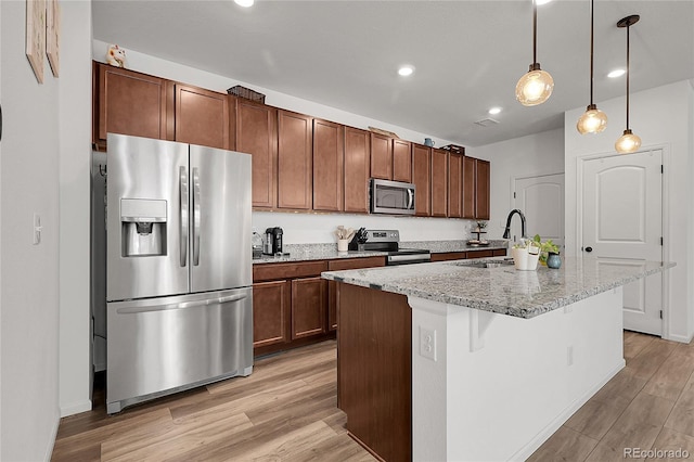 kitchen featuring a kitchen island with sink, light wood-style floors, a sink, appliances with stainless steel finishes, and hanging light fixtures