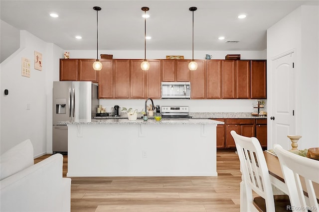 kitchen with appliances with stainless steel finishes, brown cabinetry, light wood-style flooring, visible vents, and a center island with sink