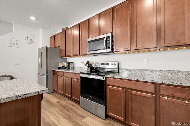 kitchen featuring light stone countertops, appliances with stainless steel finishes, brown cabinetry, light wood-style flooring, and recessed lighting
