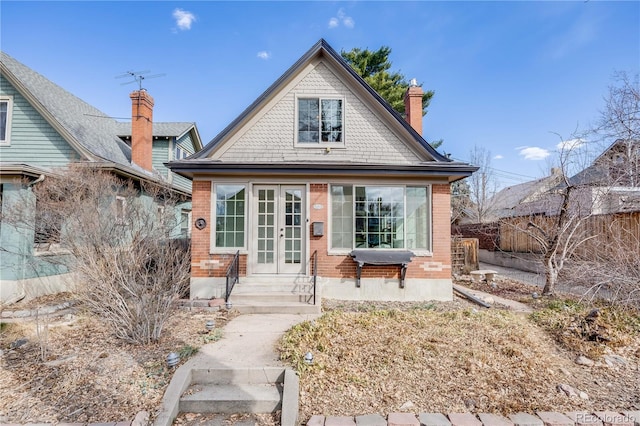 view of front of house featuring entry steps, fence, french doors, brick siding, and a chimney