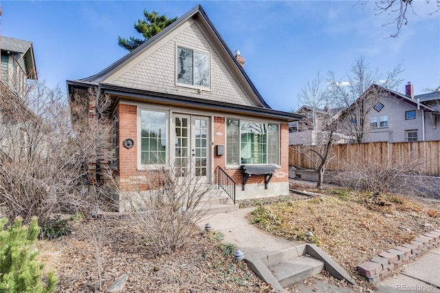 view of front facade with entry steps, fence, french doors, brick siding, and a chimney