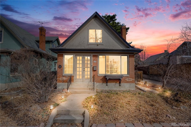 bungalow-style house featuring brick siding, french doors, and a chimney