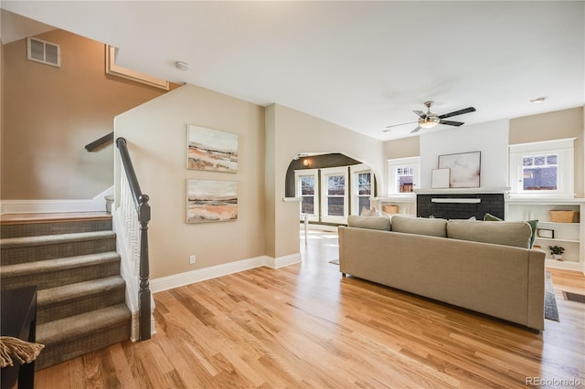 living area featuring visible vents, stairway, light wood-style floors, baseboards, and ceiling fan