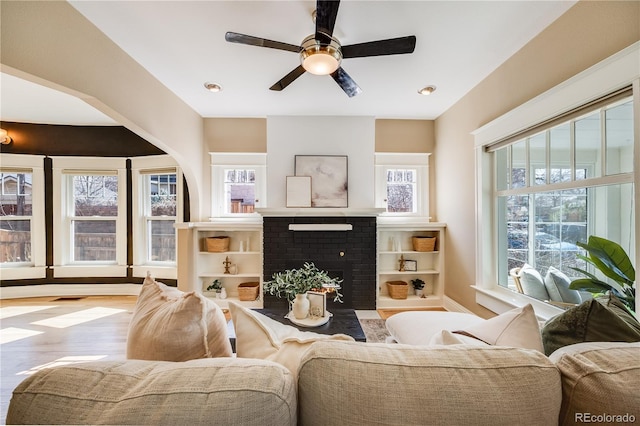 living area with a wealth of natural light, a brick fireplace, and wood finished floors