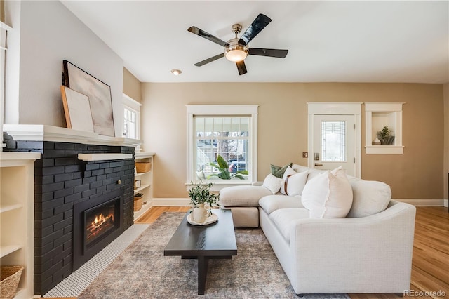 living room featuring ceiling fan, a fireplace, baseboards, and wood finished floors