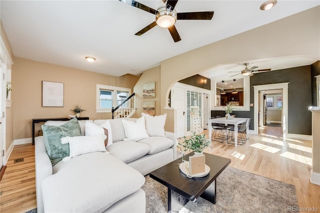 living room featuring visible vents, baseboards, stairway, light wood-style flooring, and arched walkways