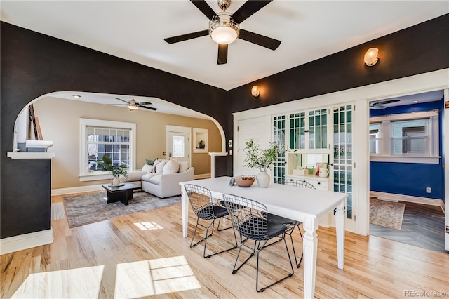 dining room featuring arched walkways, a ceiling fan, parquet floors, and baseboards