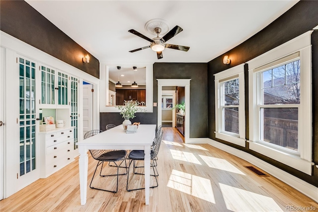 dining area featuring a ceiling fan, light wood-style floors, visible vents, and baseboards