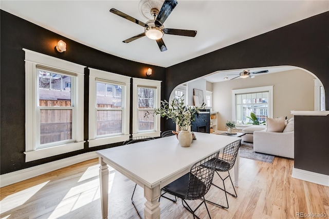 dining room with light wood-style flooring, baseboards, arched walkways, and ceiling fan