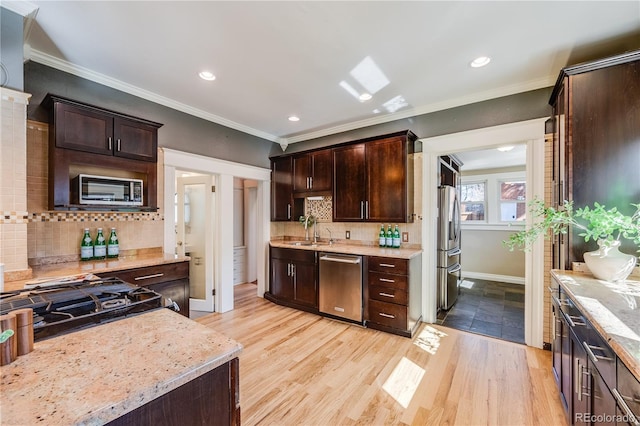 kitchen with dark brown cabinetry, stainless steel appliances, crown molding, and a sink