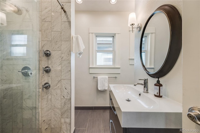 full bathroom featuring a tile shower, vanity, and baseboards