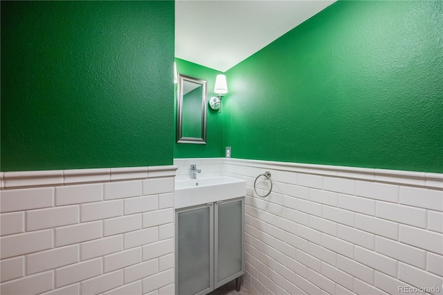 bathroom with vanity, tile walls, a textured wall, and a wainscoted wall