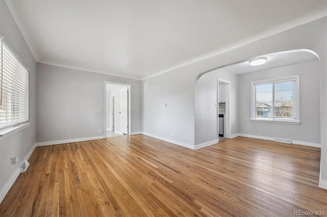 unfurnished room with arched walkways, light wood-style flooring, visible vents, and baseboards