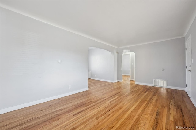 empty room featuring arched walkways, light wood finished floors, visible vents, and baseboards