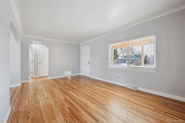 interior space featuring arched walkways, visible vents, light wood-style flooring, and baseboards