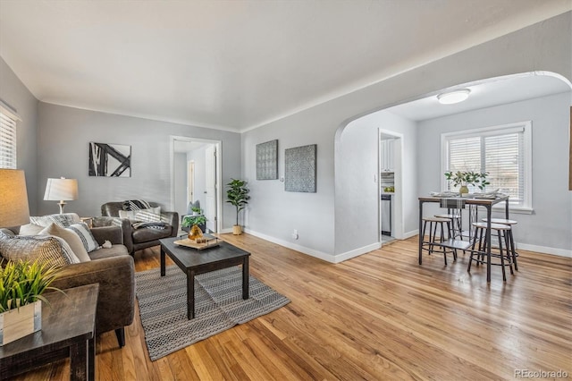 living area with light wood-type flooring, baseboards, and arched walkways