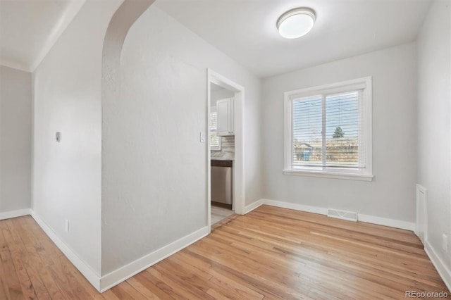 spare room featuring arched walkways, light wood finished floors, visible vents, and baseboards