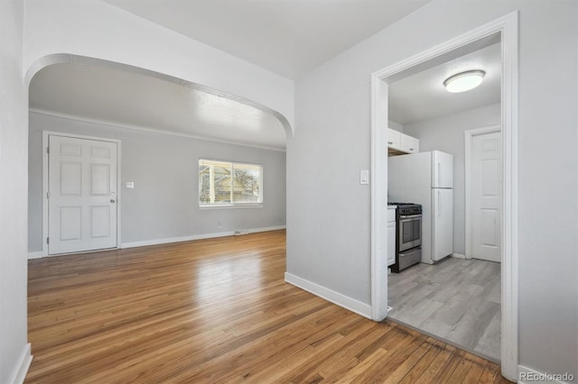 empty room featuring light wood finished floors, baseboards, and arched walkways