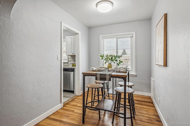 dining space featuring light wood-type flooring, a textured wall, and baseboards