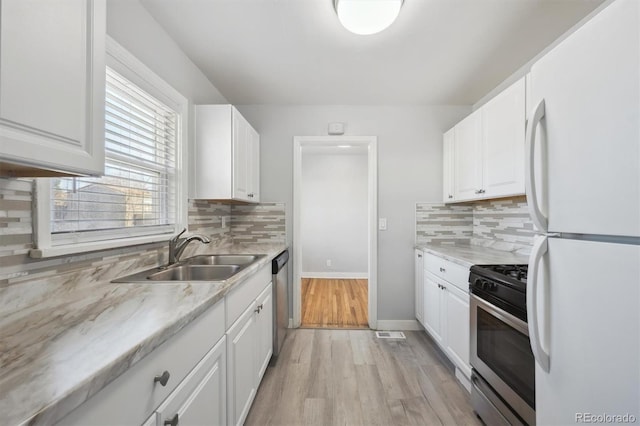 kitchen featuring stainless steel appliances, backsplash, a sink, and white cabinets