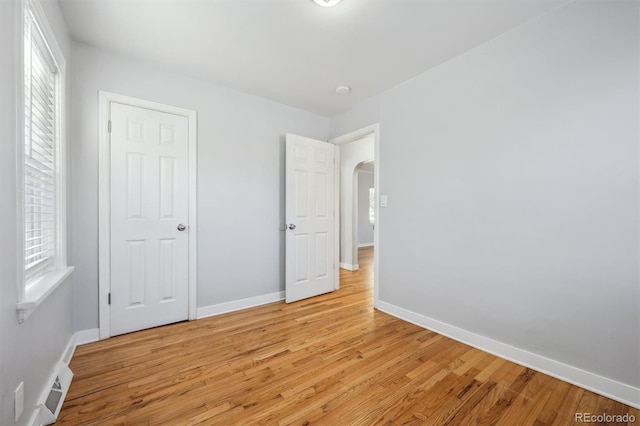 unfurnished bedroom featuring arched walkways, light wood finished floors, multiple windows, and visible vents