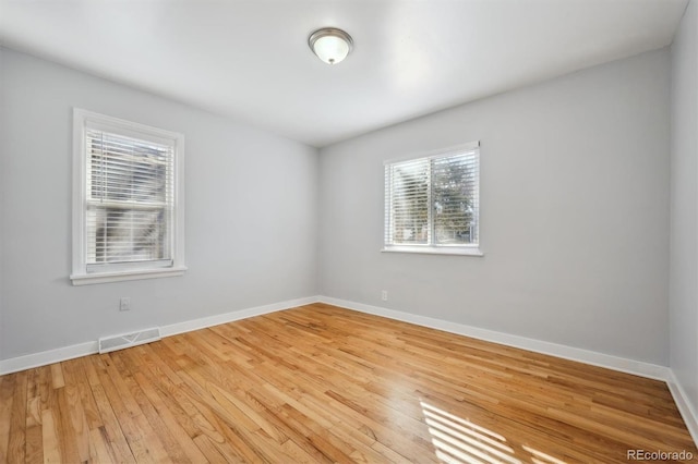 empty room featuring light wood-type flooring, visible vents, and baseboards