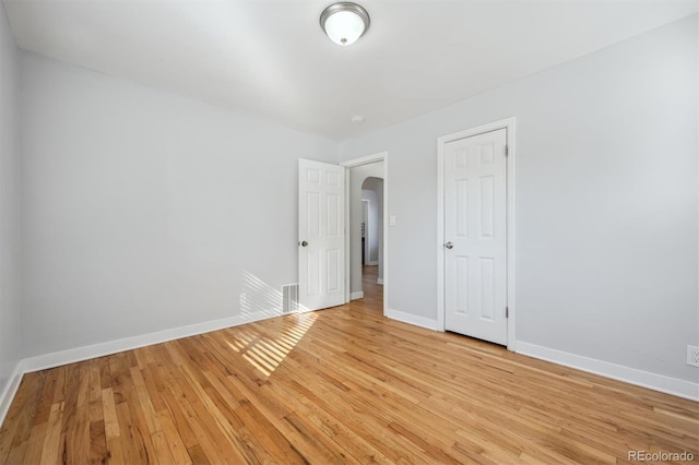 empty room with arched walkways, baseboards, visible vents, and light wood finished floors