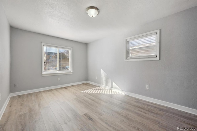 empty room with a textured ceiling, baseboards, and wood finished floors