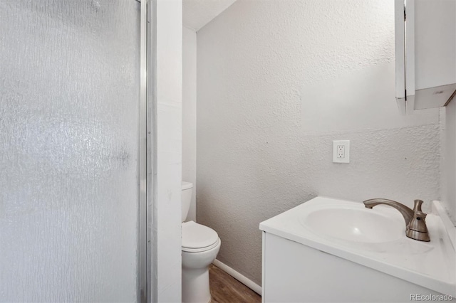 full bathroom with a textured wall, toilet, a shower stall, vanity, and wood finished floors