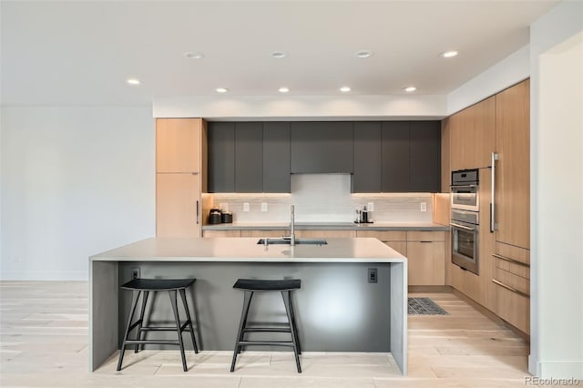 kitchen with sink, a breakfast bar area, stainless steel double oven, light hardwood / wood-style floors, and backsplash