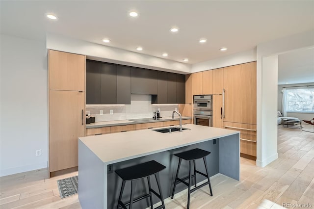 kitchen featuring sink, light hardwood / wood-style flooring, a breakfast bar area, black electric stovetop, and a center island with sink