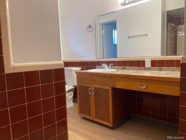 bathroom with toilet, tile walls, hardwood / wood-style floors, and vanity