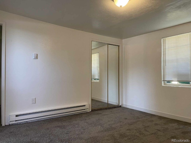 unfurnished bedroom with baseboard heating, dark carpet, a closet, and a textured ceiling