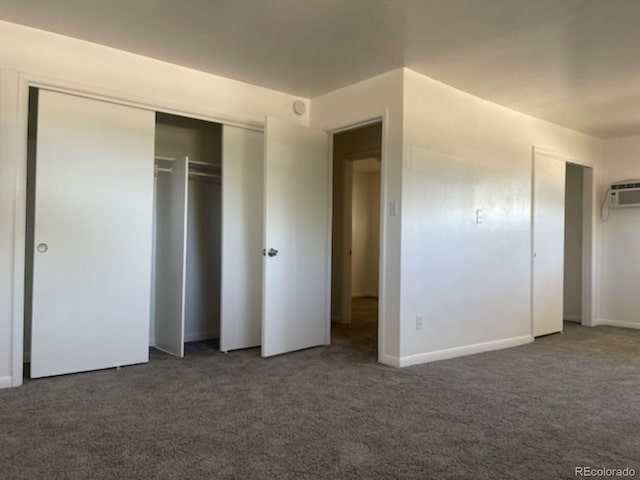 unfurnished bedroom with an AC wall unit, a closet, and dark carpet