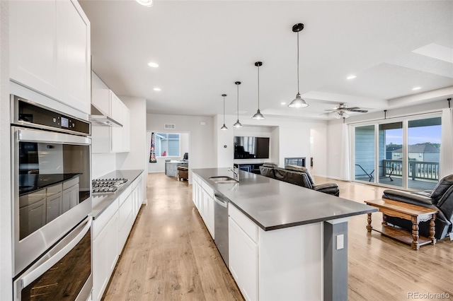 5651 Gore Creek Pl, Brighton, CO 80601 - kitchen featuring stainless steel appliances, open floor plan, dark countertops, white cabinets, and light wood-style flooring