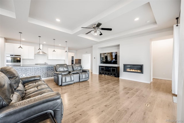 5651 Gore Creek Pl, Brighton, CO 80601 - living room featuring recessed lighting, a ceiling fan, light wood finished floors, a raised ceiling, and a glass covered fireplace
