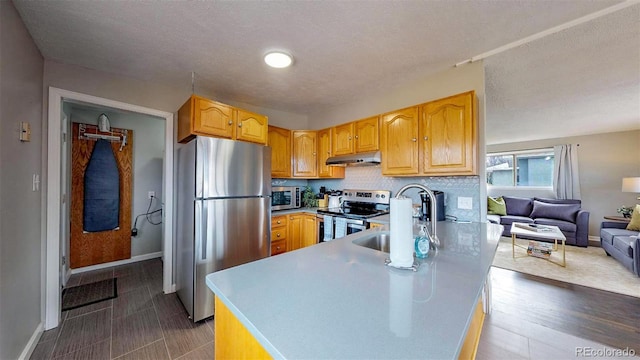 kitchen featuring dark wood-type flooring, kitchen peninsula, stainless steel appliances, a textured ceiling, and sink