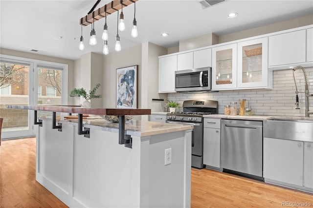 kitchen featuring backsplash, appliances with stainless steel finishes, a kitchen bar, and light wood-style floors