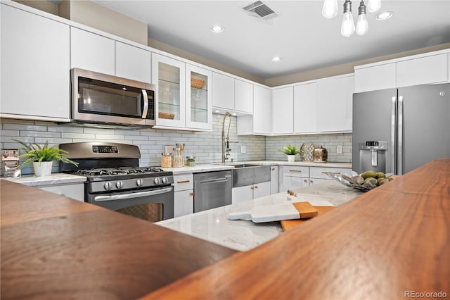 kitchen featuring visible vents, glass insert cabinets, decorative backsplash, appliances with stainless steel finishes, and white cabinetry