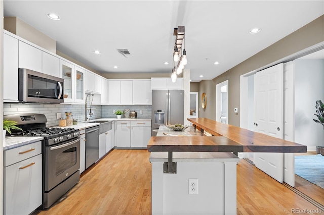 kitchen with visible vents, light wood-style flooring, a sink, stainless steel appliances, and backsplash